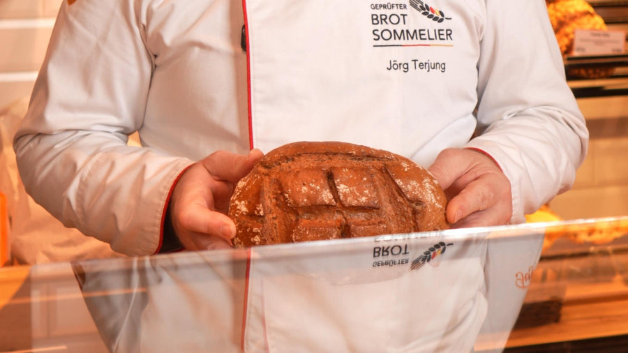 Brotsommelier Jörg Terjung mit einem Brot in der Hand hinter der Theke