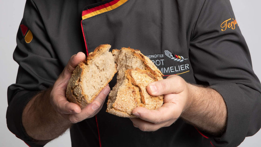 Jörg Terjung hält Brot in den Händen und hat ein schwarzes Oberteil an mit Deutschland Kragen