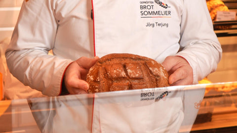 Brotsommelier Jörg Terjung mit einem Brot in der Hand hinter der Theke