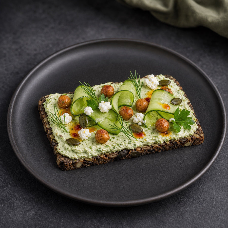 Eine einzelne Scheibe Saftkorn Kürbis-Mandel mit Kräuter-Feta-Creme, Gurkenbändern und knusprigen Kichererbsen
