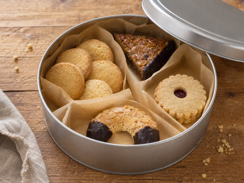 Teegebäck mit Heidesand, Nussecke, Mandelhörnchen und Linzer Törtchen in einer geöffneten Keksdose